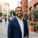 A smiling man posing for a professional portrait in a modern urban environment.