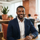 A diverse man with a friendly expression in a modern, well-lit office setting.