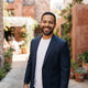 A friendly, diverse man smiling in a bright, modern urban setting with warm terracotta and burnt sienna background accents.